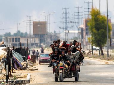 Para pria berkendara bersama di belakang gerobak roda tiga di sepanjang jalan Salaheddin, Deir el-Balah, Jalur Gaza tengah pada 21 Juli 2025, sementara di belakangnya mengepul asap akibat pemboman Israel. (Eyad BABA/AFP)