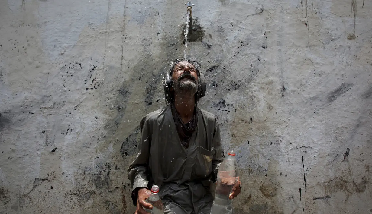 Seorang pria mendinginkan kepalanya di kucuran air keran usai mengisi botol saat cuaca panas yang ekstrem di Karachi, Pakistan, (23/6/2015). Gelombang panas yang telah menewaskan lebih dari 400 jiwa di kota selatan Pakistan. (REUTERS/Akhtar Soomro)