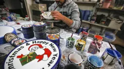 Pekerja Palestina menggambar hiasan bertema Natal di atas piring keramik di sebuah pabrik keramik di kota titik nyala Hebron di Tepi Barat (17/12/2019). (AFP/Hazem Bader)