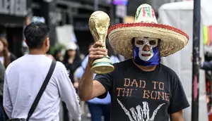 Seorang pedagang kaki lima yang mengenakan topeng gulat tradisional Meksiko memegang suvenir berbentuk trofi Piala Dunia FIFA di sebuah jalan di Kota Meksiko pada 8 Juni 2026. (Yuri CORTEZ/AFP)