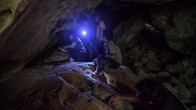 Arkeolog dari Departemen Seni Rupa melihat lukisan gua yang baru ditemukan di taman nasional Khao Sam Roi Yot di pesisir provinsi Prachuap Kiri Khan (10/9/2020). Kanniga menyorotkan senternya ke seluruh gua untuk mengungkap lukisan yang diyakini berasal dari era prasejarah. (AFP/Lillian Suwanrumpha)