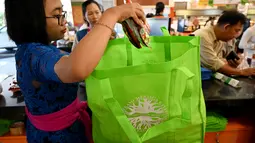 Karyawan mengemas barang belanjaan konsumen dengan tas belanja nonplastik di sebuah supermarket di Denpasar, 16 Juli 2019. Bali menerapkan pelarangan penggunaan plastik sekali pakai yang tertuang dalam Peraturan Gubernur (Pergub) Nomor 97 Tahun 2018. (SONNY TUMBELAKA/AFP)