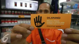 Seorang lelaki menunjukkan stiker larangan menjual rokok kepada anak di bawah usia 18 tahun, Jakarta, Rabu (30/11). Sampoerna memperkuat komitmen untuk mencegah akses penjualan rokok kepada anak-anak (Liputan6.com/Ferry Pradolo)