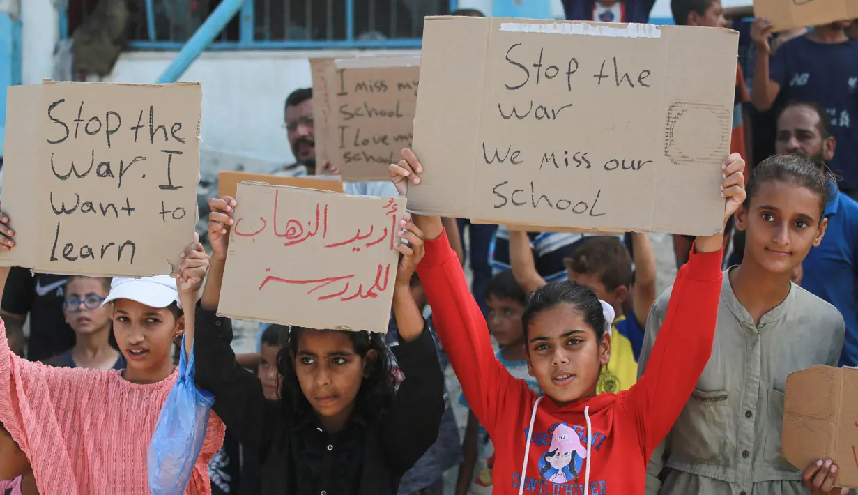 Sejumlah pelajar didampingi para aktivis Palestina mengangkat plakat saat berunjuk rasa menyerukan diakhirinya situasi perang di Gaza, di samping gedung sekolah yang rusak di Khan Yunis di Jalur Gaza selatan pada 28 Agustus 2024. (Bashar TALEB/AFP)