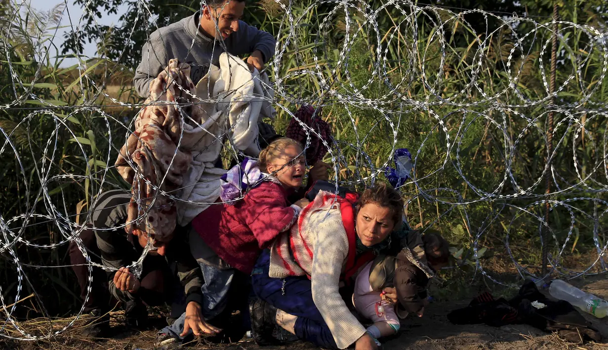 Sejumlah imigran Suriah menyeberangi bawah pagar berduri untuk memasuki negara Hungaria di perbatasan Serbia, 27 Agustus 2015. (REUTERS/Bernadett)