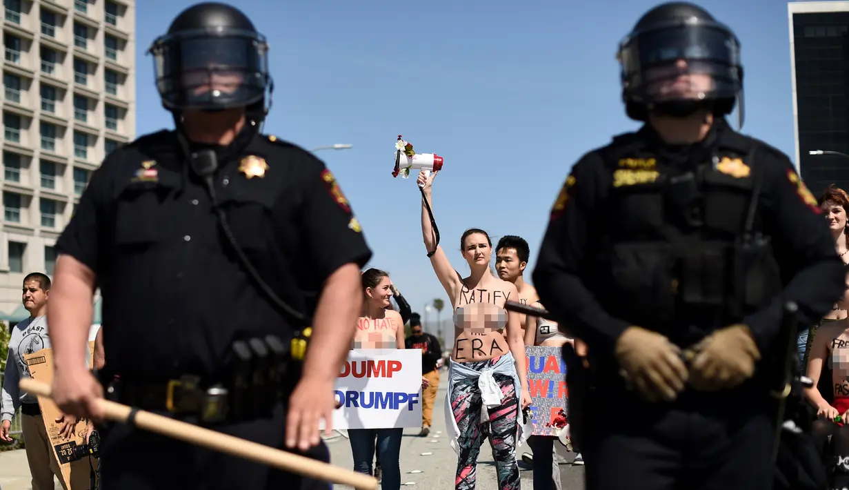 Petugas berjaga saat sejumlah wanita bertelanjang dada menolak Donald Trump di Burlingame, California (29/4). Demonstran menggelar aksi di depan Hotel Hyatt, lokasi Donald Trump melakukan kampanye Pilpres AS. (REUTERS/Noah Berger)