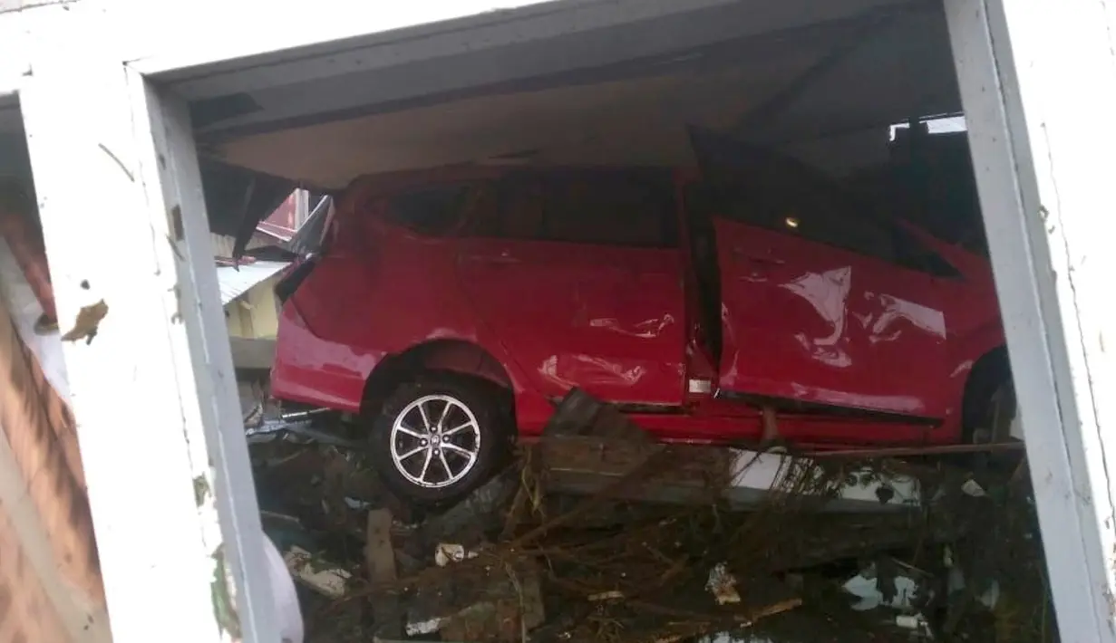 Sebuah mobil yang tersapu oleh tsunami terlihat terjebak di bawah bangunan yang rusak di Palu, Sulawesi Tengah , Sabtu (29/9). Gelombang tsunami yang menerjang Palu terjadi setelah gempa bumi mengguncang Palu dan Donggala. (Dede Budiyarto via AP)