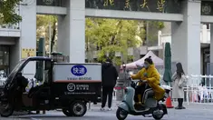 Seorang perempuan yang mengenakan masker melewati pintu masuk Universitas Peking di Beijing, Rabu (16/11/2022). Pihak berwenang China mengunci Universitas Peking setelah temuan satu kasus virus Corona Covid-19 di area kampus. (AP Photo/Ng Han Guan)