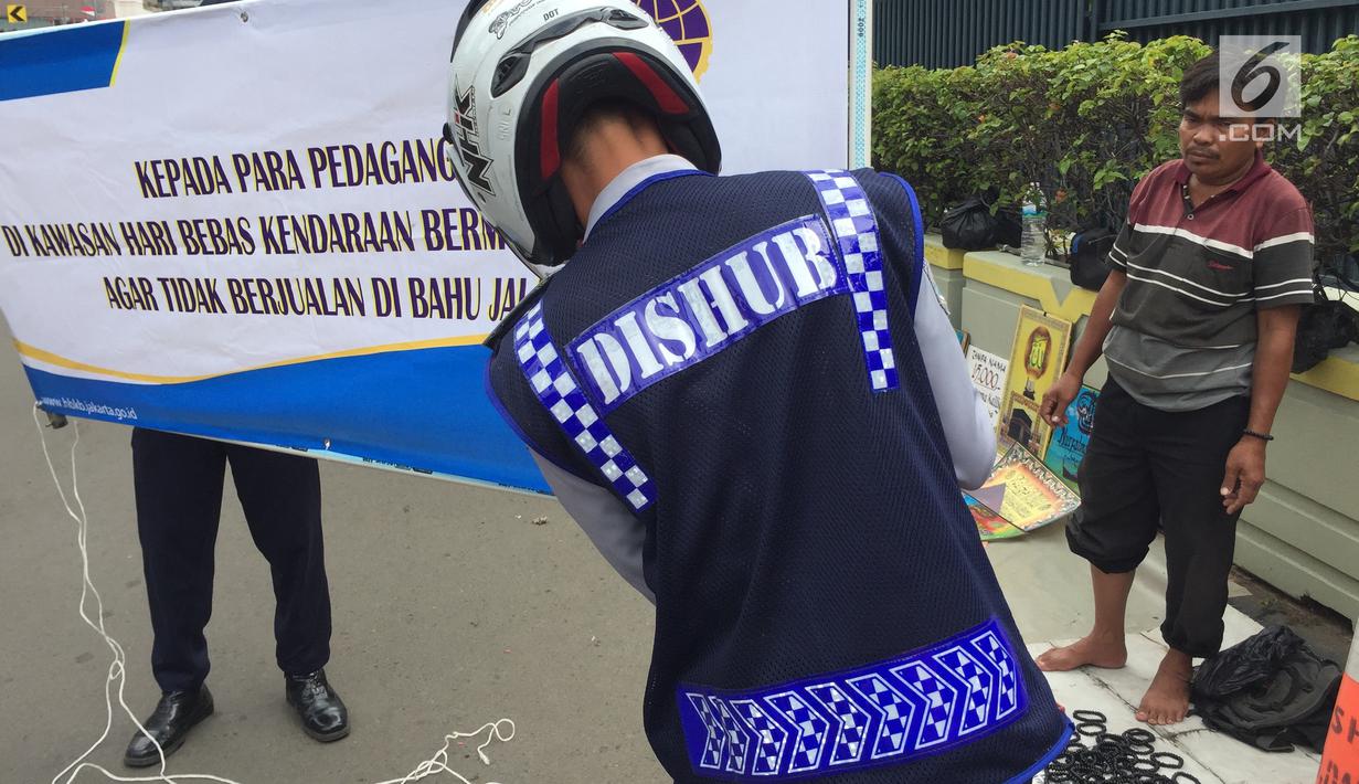 Petugas bersiap memasang spanduk larangan bagi PKL yang menggelar lapak dagangan saat CFD di Jakarta, Minggu (11/2). Pasalnya, mereka menggelar lapak dagangannya di bahu jalan. (Liputan6.com/Immanuel Antonius)