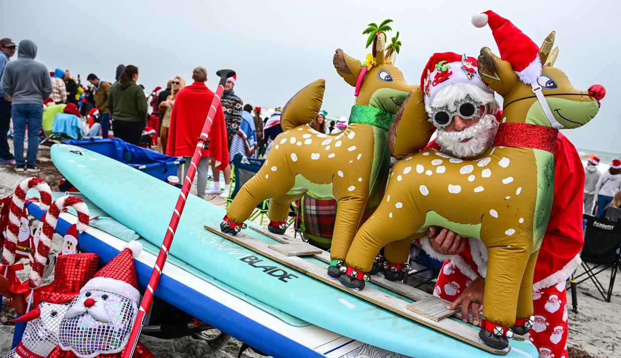 Seorang pengunjung berkostum Sinterklas berpose dalam acara Surfing Santa yang berlangsung di Pantai Cocoa, Florida, Amerika Serikat, Selasa (24/12/2024) waktu setempat. (AFP/Giorgio Viera)