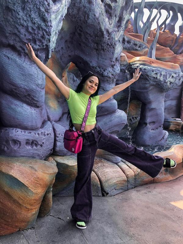 Perpaduan kaos dan kaos kaki hijau, serta celana berwarna ungu dan sling bag merah muda menjadi pilihan Sheryl saat berkunjung ke Tokyo Disney Sea. Senyum manis juga ditunjukan oleh Sheryl pada unggahan foto tersebut. (Liputan6.com/IG/@sherylsheinafia)