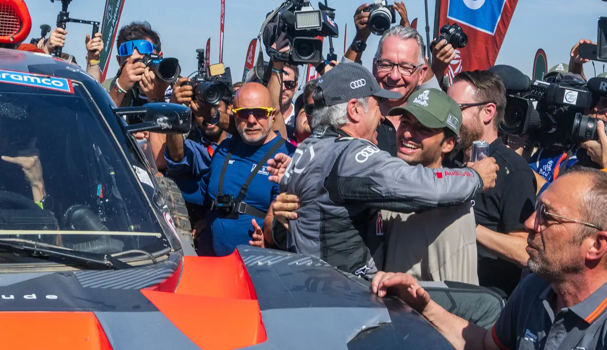 Pembalap Team Audi Sport, Carlos Sainz (tengah kiri) mendapatkan pelukan dari sang anak, yang juga seorang pembalap Formula 1, Carlos Sainz Jr saat memenangkan Reli Dakar 2024 setelah menyelesaikan etape terakhir di Yanbu, Arab Saudi, Jumat, 19 Januari 2024 waktu setempat. (AFP/Patrick Hertzog)