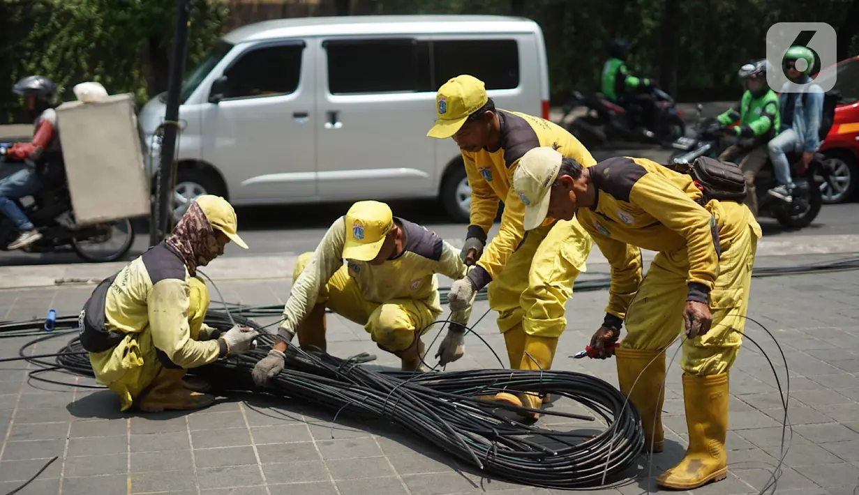 Petugas Bina Marga merapikan kabel optik yang baru saja dipotong di sepanjang jalan kawasan Kemang, Jakarta, Kamis (24/10/2019). Pemotongan kabel optik tersebut untuk menertibkan instalasi kabel yang semrawut serta mengganggu ketertiban umum di kawasan Kemang. (Liputan6.com/Immanuel Antonius)