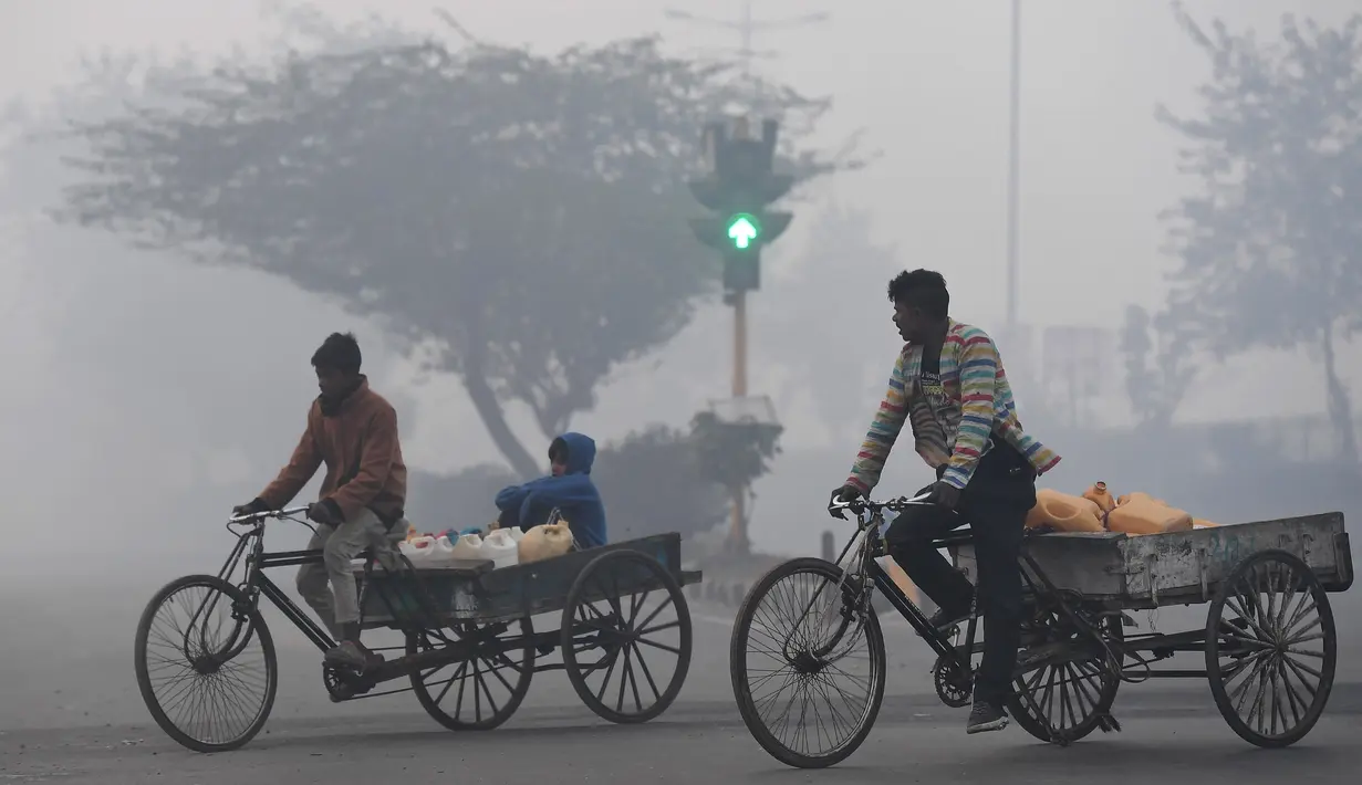 Pria India mengayuh becak roda tiga membawa air minum di tengah kabut tebal di New Delhi (25/12). India ditetapkan darurat polusi udara. Kualitas udara yang semakin buruk dan kabut beracun menyelimuti. (AFP Photo/Prakash Singh)