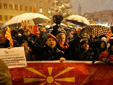 Warga membentangkan bendera Macedonia saat menggelar protes di depan gedung Parlemen, Skopje, Selasa (27/2). Di tengah hujan salju dan temperatur ekstrem, mereka turun ke jalan memprotes wacana pengubahan nama negara mereka. (AP/Boris Grdanoski)