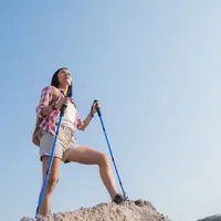 Seorang perempuan berdiri di atas sebuah gunung dengan memegang dua tongkat tracking (Foto Dok: Freepik/jcomp).