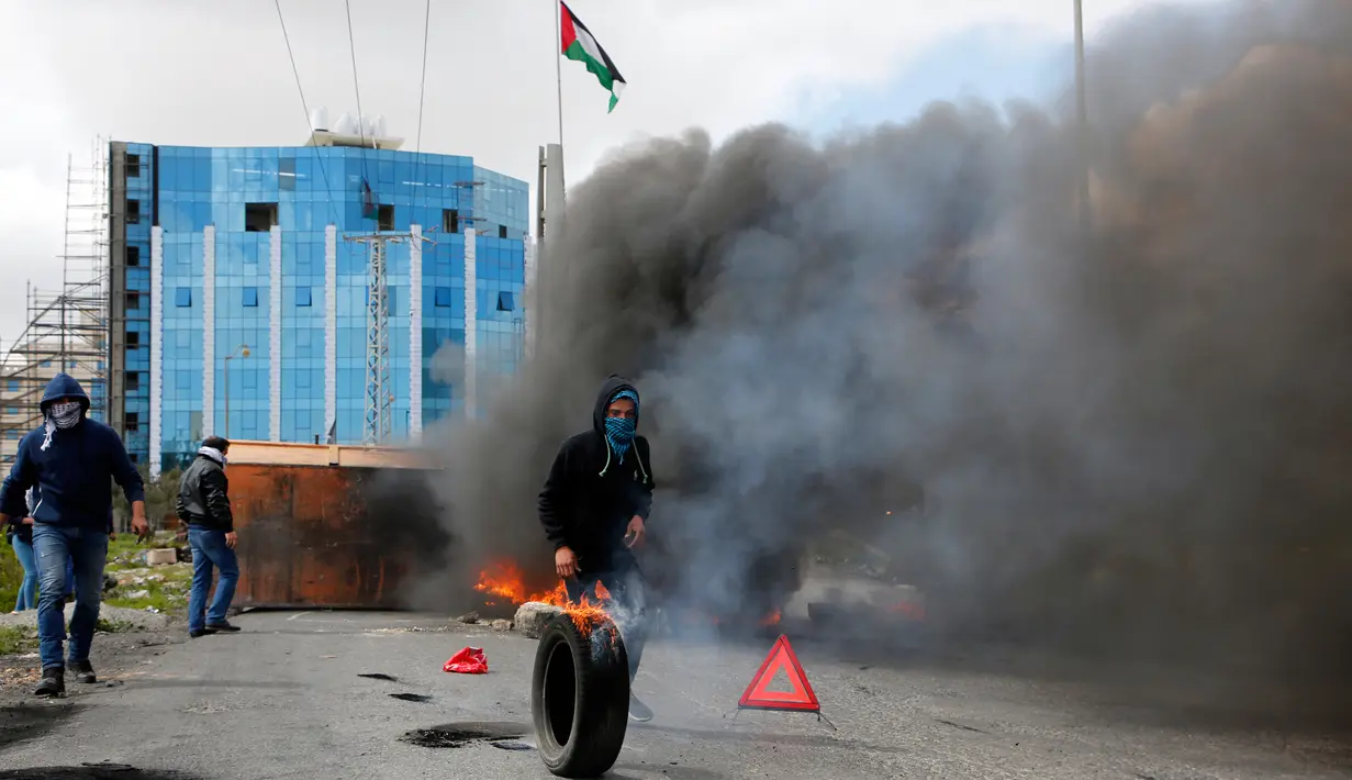 Demonstran Palestina membakar ban saat terjadi bentrokan menyusul demonstrasi di kota Ramallah Palestina (16/3). Mereka melakukan aksi menolak Yerusalem sebagai ibu kota Israel. (AFP Photo/Abbas Momani)