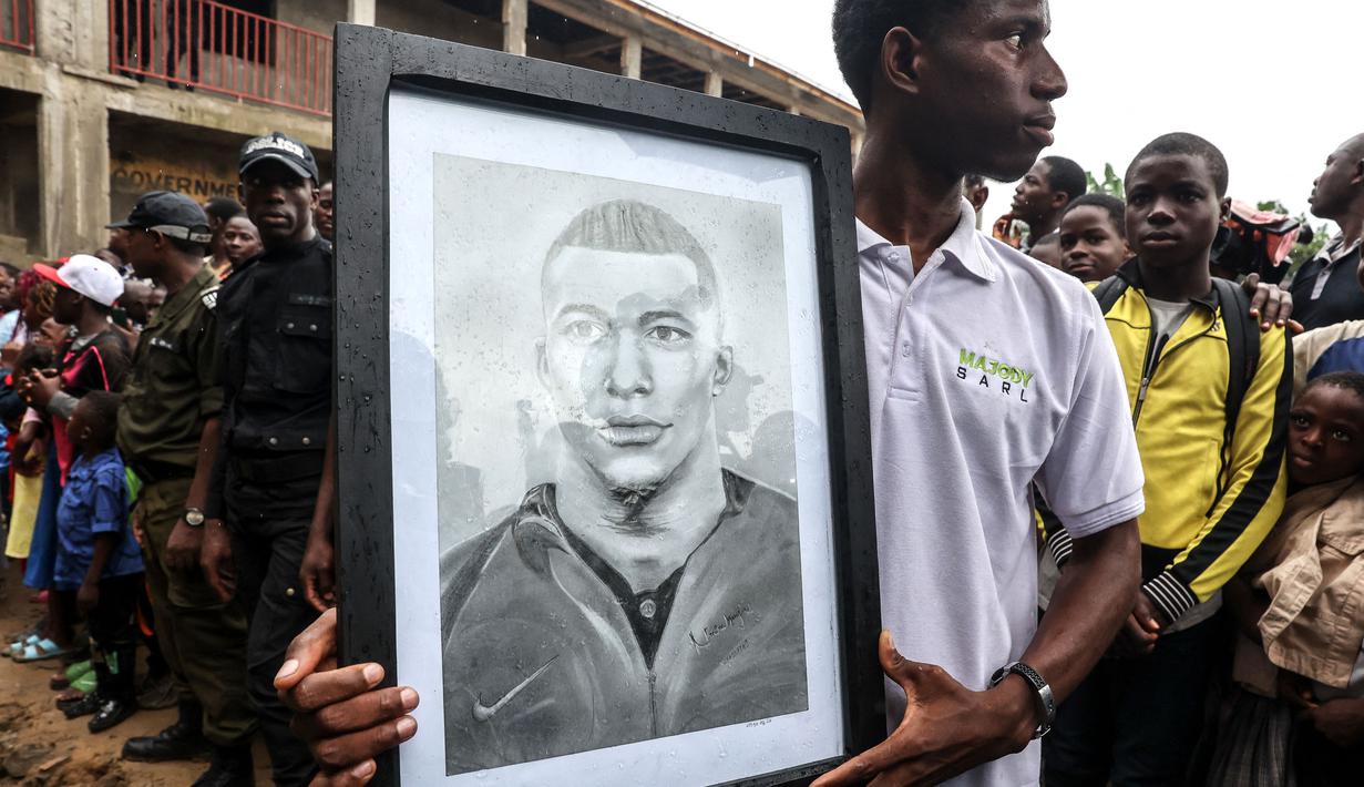Seorang penduduk setempat memegang potret pemain Paris Saint-Germain sekaligus kapten Timnas Prancis, Kylian Mbappe yang mengunjungi sekolah umum dwibahasa Bonendale, yang direnovasi oleh yayasan Inspired By Kylian Mbappe Foundation (IBKM), di Douala pada 8 Juli 2023. (AFP/Daniel Beloumou Olomo)