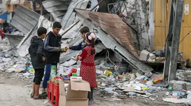 Anak-anak Palestina berjualan manisan pada hari kelima gencatan senjata sementara antara Hamas dan Israel di depan reruntuhan bangunan kamp pengungsi Jebaliya, Jalur Gaza, 28 November 2023. (AP Photo/Mohammed Hajjar)