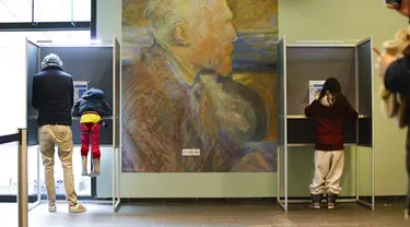 Seorang pria bersama anaknya (kiri) memberikan suara di bilik suara dalam pemilihan umum di Museum Van Gogh, Amsterdam, Belanda, Rabu (17/3/2021). Pemilu digelar selama tiga hari untuk memungkinkan warga memilih dengan aman selama pandemi virus corona COVID-19. (AP Photo/Peter Dejong)