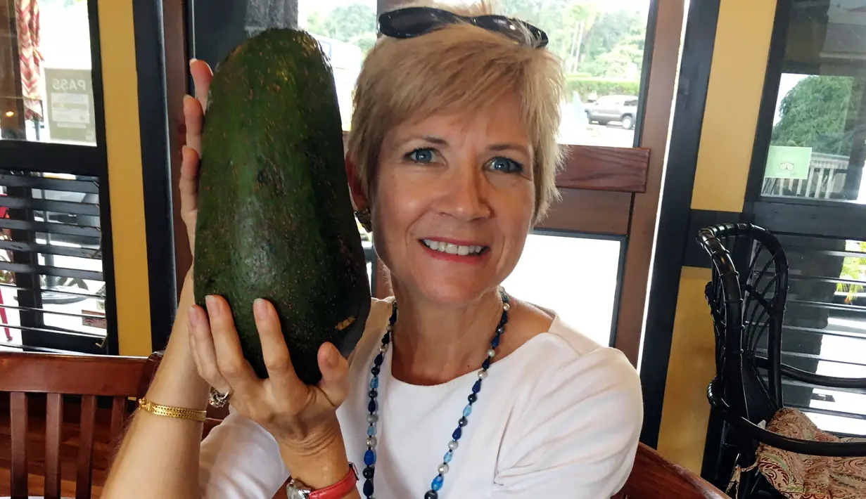 Dalam foto 28 November 2017 memperlihatkan seorang wanita Hawaii, Pamela Wang berpose dengan buah alpukat super jumbo yang ditemukannya di Kealakekua. Pamela menemukan alpukat seberat 2,3 kg yang seukuran dengan kepalanya. (AP Photo/Mary Lou Knurek)