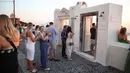 Wisatawan mengantri menunggu untuk berfoto dari salah satu balkon dengan pemandangan laut dan matahari terbenam di Fira di pulau Santorini Yunani pada 19 Juli 2024. Aris Oikonomou / AFP)