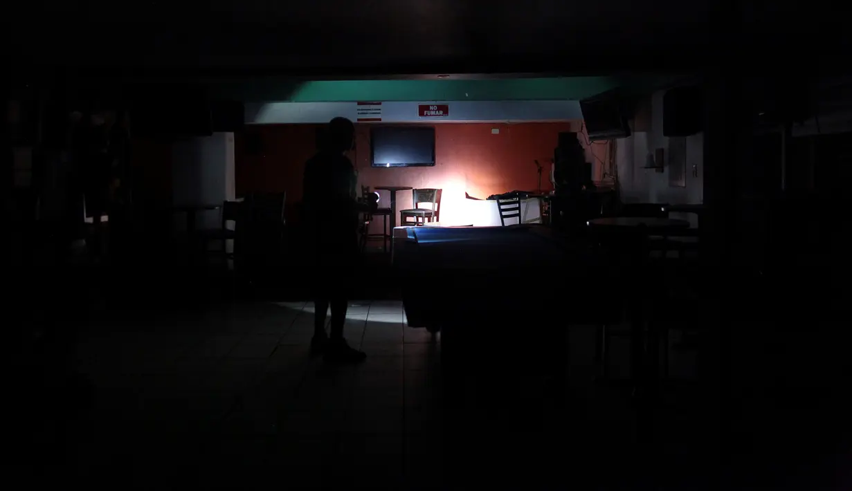 Seorang pria menggunakan senter ketika terjadi pemadaman listrik di tokonya di San Juan, Puerto Rico, Rabu (21/9). Kebakaran telah memutus dua jalur transmisi listrik dan mengakibatkan kegagalan penyaluran tenaga ke seluruh pulau. (REUTERS/Alvin Baez)