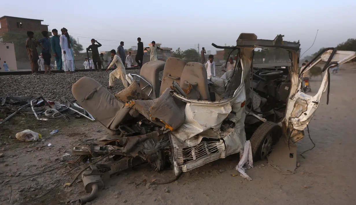 Warga berkumpul dekat puing-puing bus yang tertabrak kereta api di Farooq Abad, Distrik Sheikhupura, Pakistan, Jumat (3/7/2020). Kecelakaan tersebut mengakibatkan 22 orang tewas. (AP Photo/K.M. Chaudary)