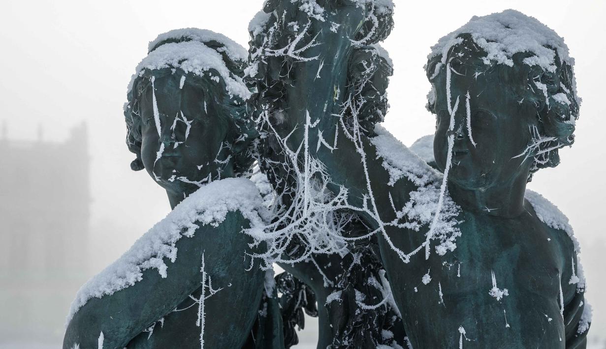 Pemandangan serba putih ini menciptakan suasana romantis bagi para wisatawan yang mengabadikan momen di ikon Kota Paris. Tampak dalam foto, salju menyelimuti sebuah patung di taman Versailles, luar Kota Paris pada Selasa 6 Januari 2026. (GEOFFROY VAN DER HASSELT/AFP)