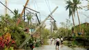 Sejumlah warga berjalan dibawah tiang listrik yang roboh akibat angin kencang yang disebabkan Topan Nock-ten di Kota Iriga Camarines Sur, Filipina tengah (27/12). (REUTERS/Romeo Ranoco)