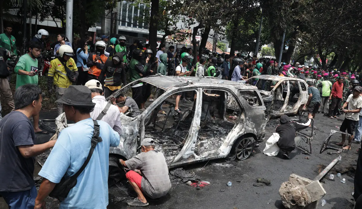 Warga melihat sisa mobil yang dibakar massa ketika aksi unjuk rasa menuntut pengusutan kasus penabrakan pengemudi ojek online di sekitar Markas Komando Korps Brigade Mobil (Brimob) Polda Metro Jaya, kawasan Kwitang, Pasar Senen, Jakarta, Jumat (29/8/2025). (merdeka.com/Arie Basuki)