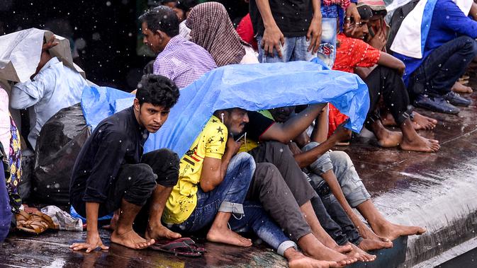 Warga Bangladesh melindungi diri mereka dari hujan saat duduk di atas atap kereta untuk menuju kampung halaman di Dhaka pada 4 Juni 2019. Sebagaimana terjadi di Indonesia, masyarakat Bangladesh pun memiliki tradisi mudik saat Idul Fitri, namun agak membahayakan keselamatan. (MUNIR UZ ZAMAN/AFP)