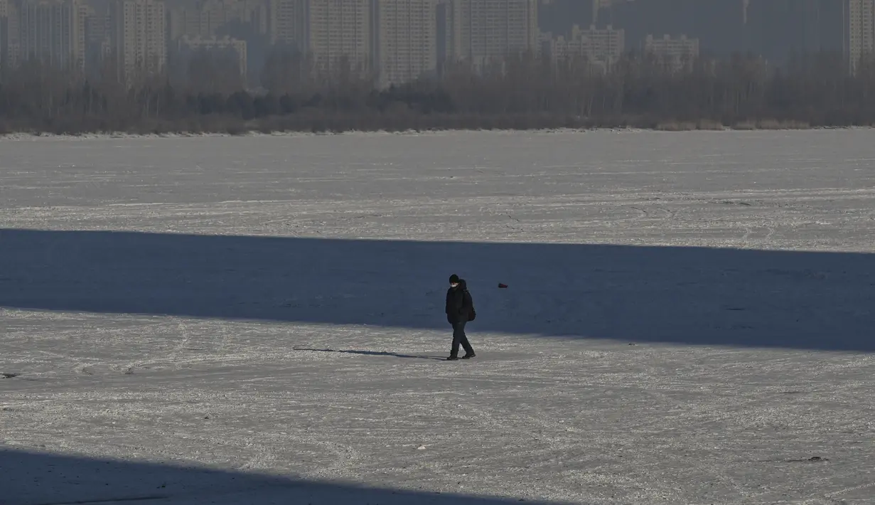 Seorang pria berjalan di sungai beku di Harbin, di provinsi Heilongjiang timur laut China, pada 4 Januari 2023, menjelang Festival Es dan Salju Internasional Harbin China ke-39. (AFP/Hector Retamal)