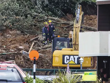 Polisi dan petugas yang berdiri setelah tanah longsor sementara pencarian sedang dilakukan oleh layanan darurat setempat untuk orang hilang di Gunung Maunganui, Tauranga, Selandia Baru pada Kamis 22 Januari 2026. Hujan lebat yang mengguyur Selandia Baru menyebabkan sejumlah kerusakan dan memicu longsor. (DJ MILLS/AFP)