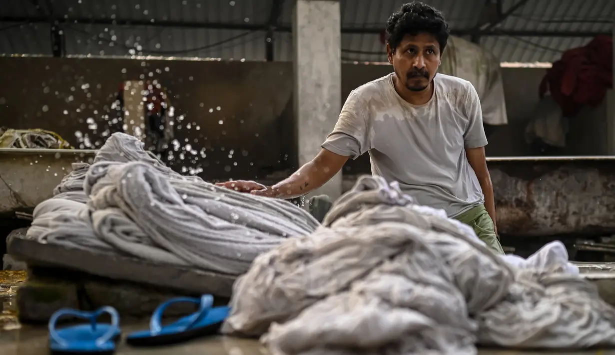 Seorang tukang cuci mencuci pakaian di binatu terbuka, yang secara lokal disebut 'Dhobi Ghat' di New Delhi, India pada 14 Maret 2022. Dhobi Ghat adalah tempat yang menyediakan layanan cuci dengan cara tradisional. (Money SHARMA / AFP)