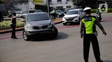 Petugas polisi mengarahkan kendaraan berplat nomor genap di pos penyekatan ganjil-genap di Bundaran Senayan, Minggu (5/9/2021). Pembatasan kendaraan dengan sistem pelat nomor kendaraan ini tetap berlaku di akhir pekan, Sabtu dan Minggu. (Liputan6.com/Angga Yuniar)