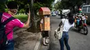 Orang-orang mengambil gambar pensiunan perawat, Feridia Rojas yang memakai kotak kardus berbentuk rumah untuk melindungi dirinya dari penyebaran Covid-19 di Havana, Kuba, 8 Juli 2020. Pakaian pelindung kardus itu dipakai Rojas untuk melakukan aktivitas di luar rumah sehari-hari. (AP/Ramon Espinosa)