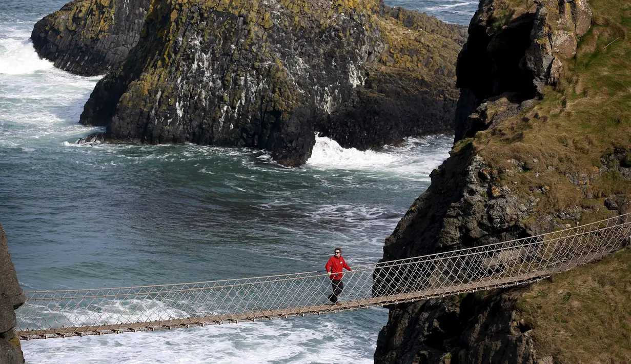 Seorang wisatawan berdiri di tengah Jembatan Carrick-a-Rede Rope di Pantai Causeway, Irlandia Utara, Rabu (8/4/2015). Jembatan tersebut diperkirakan telah dibangun selama lebih dari 350 tahun oleh para nelayan salmon. (REUTERS/Cathal McNaughton)