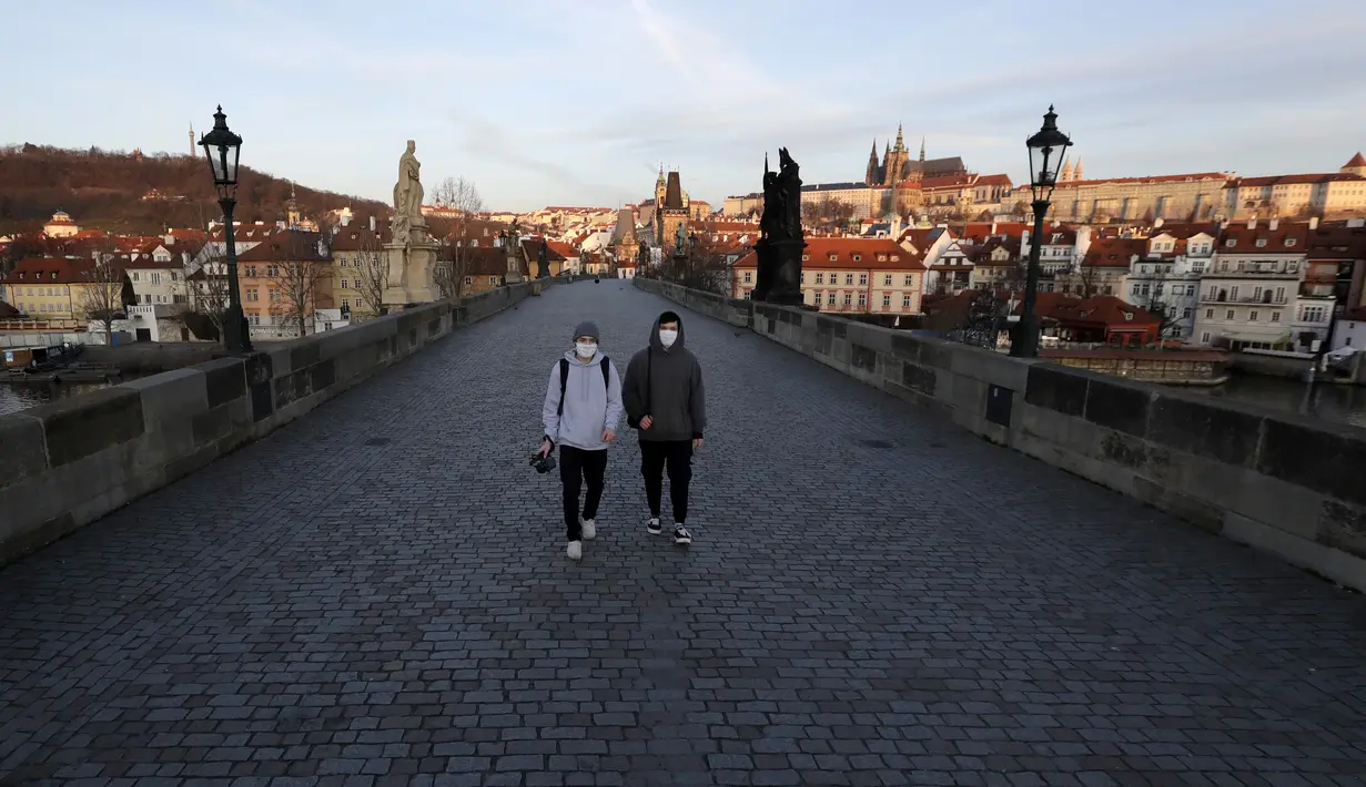 Dua pria muda yang mengenakan masker berjalan melintasi Jembatan Charles yang sepi di Praha, Republik Ceko, Senin (16/3/2020). Pemerintah Ceko memberlakukan pembatasan terhadap seluruh warganya dalam upaya mengendalikan penyebaran virus corona COVID-19. (AP Photo/Petr David Josek)