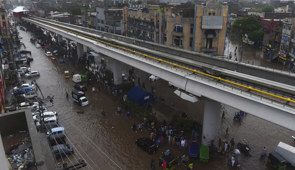 Sejumlah warga beraktivitas di bawah jembatan komuter line yang banjir setelah hujan lebat di Lahore (16/7/2019). Di Kashmir yang dikelola Pakistan, para pejabat pemerintah mengatakan sedikitnya 23 orang tewas setelah hujan lebat memicu banjir bandang. (AFP Photo/Arif Ali)