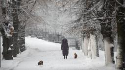 Seorang perempuan berjalan dengan anjing melewati taman yang tertutup salju setelah hujan salju lebat di Vilnius, Lituania, Jumat, 9 Desember 2022. Lituania, Jumat, 9 Desember 2022. Salju terus turun di seluruh negeri, dengan suhu hanya 0 derajat Celcius (32,0 derajat Fahrenheit). (AP Photo/Mindaugas Kulbis)