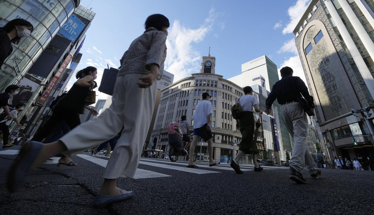 Warga yang mengenakan masker untuk membantu mengekang penyebaran COVID-19 berjalan di sepanjang penyeberangan pejalan kaki di Tokyo, Jepang, Selasa (27/7/2021). Tokyo melaporkan jumlah kasus harian COVID-19 tertinggi beberapa hari setelah Olimpiade dimulai. (AP Photo/Eugene Hoshiko)