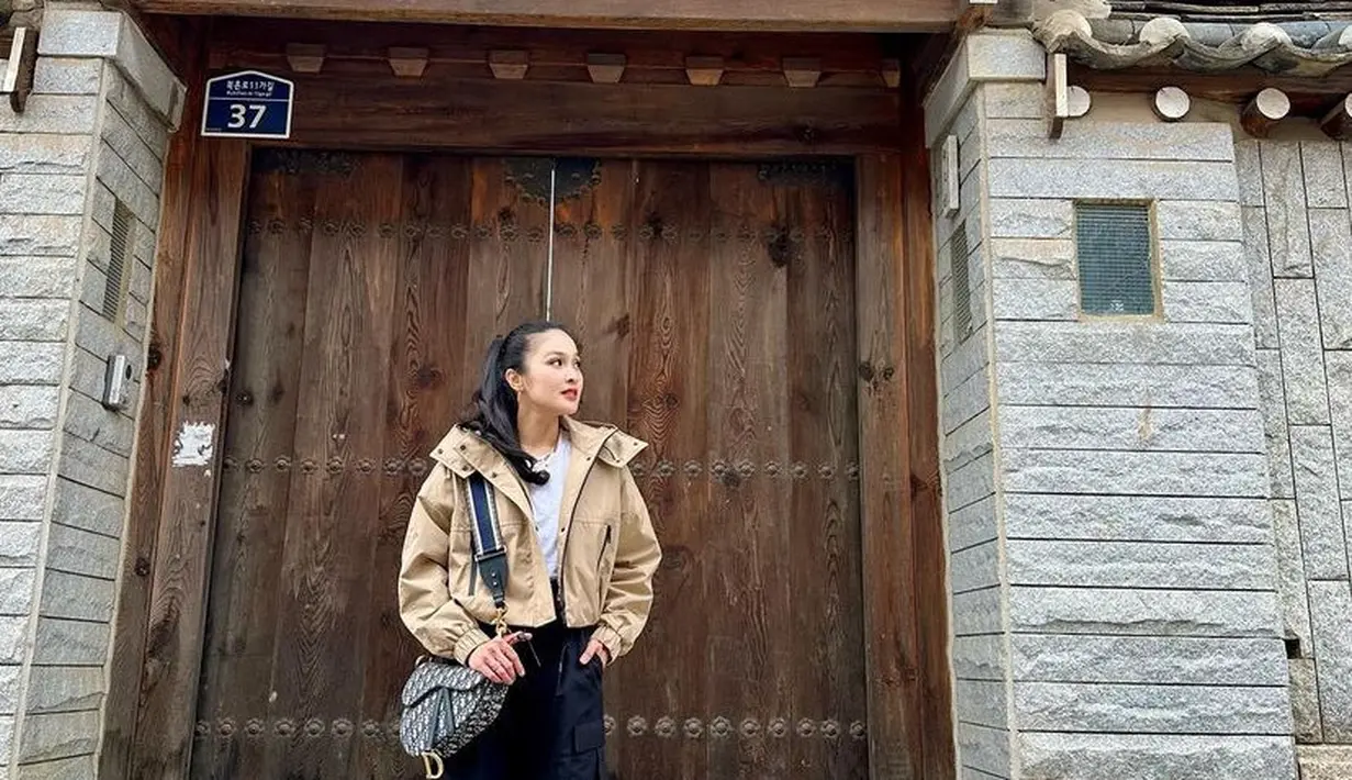 Berkunjung ke Bukchon Hanok Village, Sandra Dewi memilih mengenakan jaket beige crop top dipadukan inner putih dan celana cargo hitam serasi dengan boots dan sling bag Dior. [@sandradewi88]
