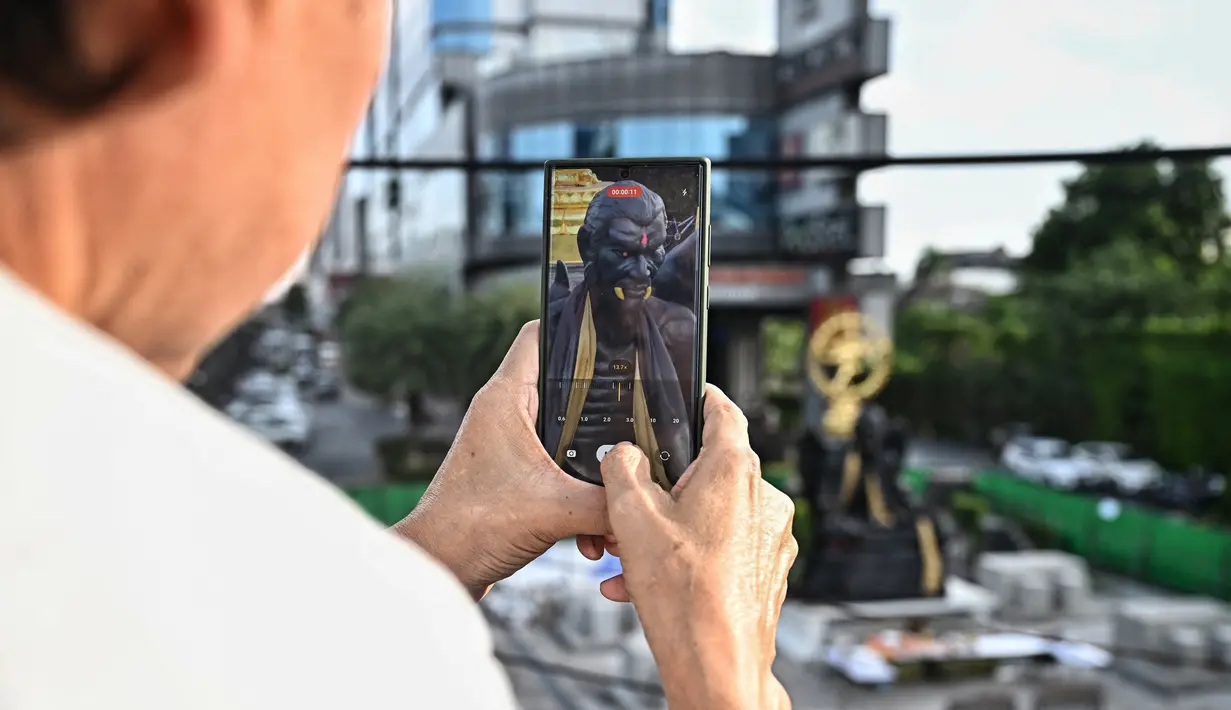 Seseorang mengambil foto patung raksasa dewa Kru Kai Kaew, yang dianggap oleh beberapa orang sebagai "dewa kekayaan" tetapi oleh yang lain dianggap asing bagi agama Buddha, di Bangkok, Thailand pada 18 Agustus 2023. (Lillian SUWANRUMPHA / AFP)