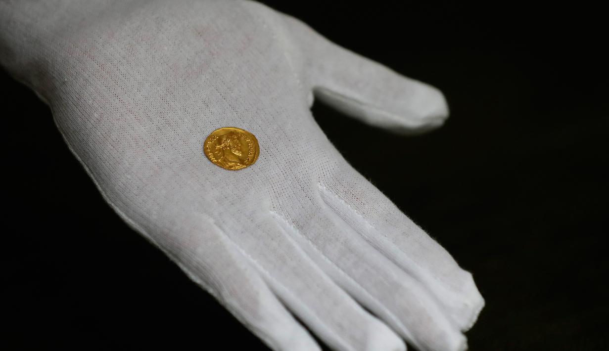 Seorang karyawan Dix Noonan Webb menunjukkan koin Romawi kuno di London, Inggris (28/5/2019). Koin emas ini berasal dari tahun 293-296 M yang ditemukan di sebuah lapangan di Kent, Inggris. (AP Photo/Kirsty Wigglesworth)