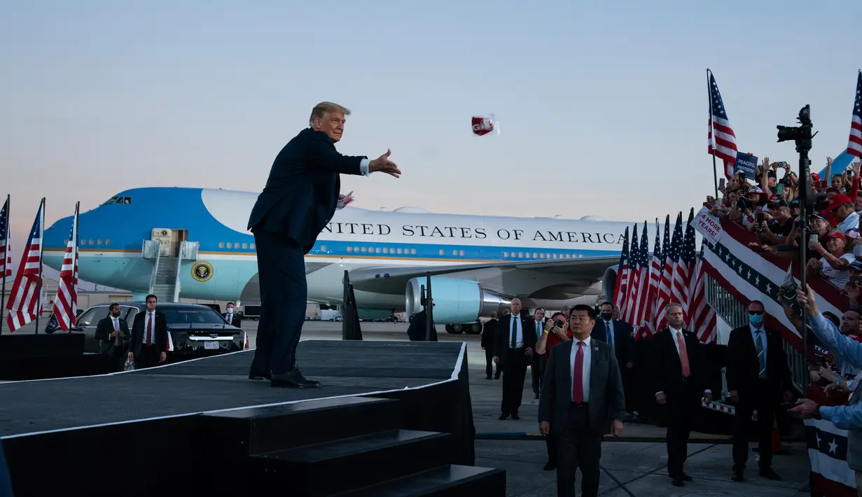 Presiden Donald Trump melemparkan masker dari atas panggung ke kerumunan pendukung saat berkampanye di Bandara Internasional Orlando Sanford di Sanford, Florida, Senin (12/10/2020). Donald Trump kembali berkampanye untuk pertama kalinya usai dinyatakan negatif Covid-19. (AP Photo/Evan Vucci)