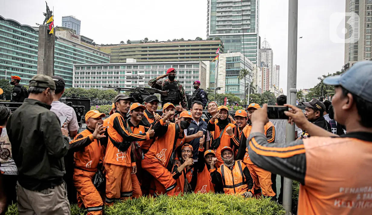 Petugas Penanganan Prasarana dan Sarana Umum (PPSU) berfoto dengan tentara dan alat utama sistem senjata (alutsista) milik TNI saat perayaan HUT ke-77 TNI di Bundaran HI, Jakarta, Rabu (5/10/2022). Kegiatan yang diikuti oleh seluruh kesatuan jajaran TNI ini dalam rangka menyambut HUT ke-77 TNI. (Liputan6.com/Faizal Fanani)