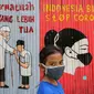 Seorang anak kenakan masker dengan latar belakang mural Indonesia Bisa Stop Corona di Lapangan Bulutangkis, Kampung Kali Pasir, Jakarta, Selasa (7/4/2020). Pesan mural mengajak warga untuk memutus rantai penyebaran Corona Covid-19 dengan diam di rumah. (Liputan6.com/Fery Pradolo)