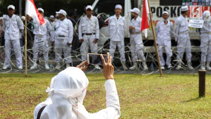Seorang wanita mengambil gambar Massa Forum Umat Islam yang mengikuti 'Apel Siaga Umat untuk Pemilu Bersih, Jujur, dan Adil' di depan Kantor KPU, Jakarta, Minggu (31/3). Massa menolak segala bentuk kecurangan dalam Pemilu yang akan berlangsung 17 April mendatang. (Liputan6.com/Immanuel Antonius)