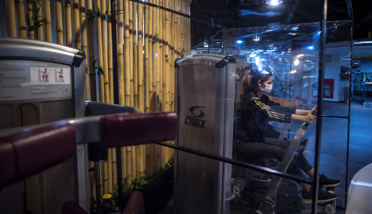 Orang-orang berolahraga dengan plastik penyekat untuk membatasi jarak antar pengunjung di sebuah tempat gym di Surabaya, Rabu (21/10/2020). Pusat kebugaran itu dibuka dengan menerapkan protokol kesehatan sebagai pencegahan COVID-19. (Juni Kriswanto / AFP)